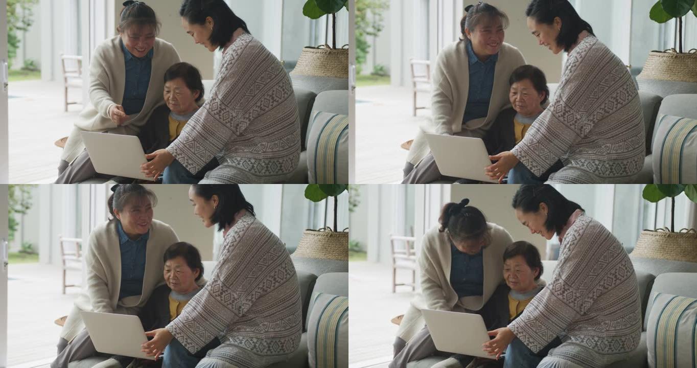 快乐的亚洲资深母亲、成年女儿和孙女坐在客厅使用笔记本电脑