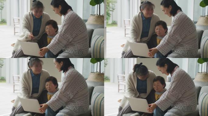 快乐的亚洲资深母亲、成年女儿和孙女坐在客厅使用笔记本电脑