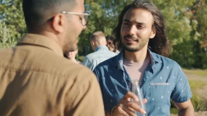 快乐帅哥的肖像阿拉伯人从瓶子里喝酒，在公园里享受露天派对