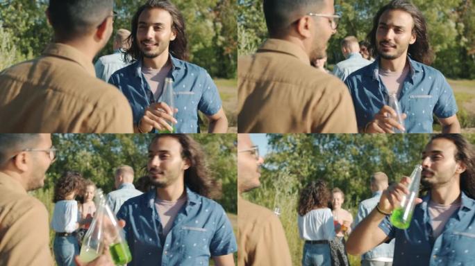 快乐帅哥的肖像阿拉伯人从瓶子里喝酒，在公园里享受露天派对