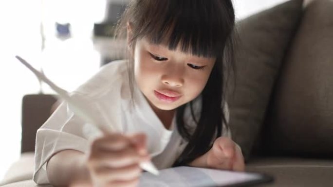 小女孩在家中在数字平板电脑上写作以进行电子学习
