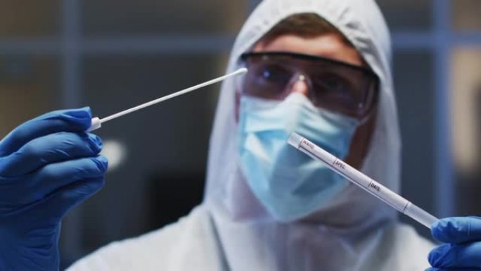 白种人男性医务人员戴着防护服口罩和手套在实验室检查dna拭子