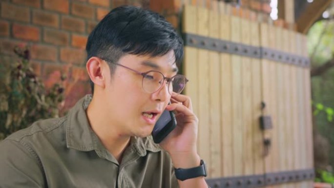 特写亚洲自由职业者戴着眼镜在电话上聊天，使用笔记本电脑。多任务和远程工作概念。