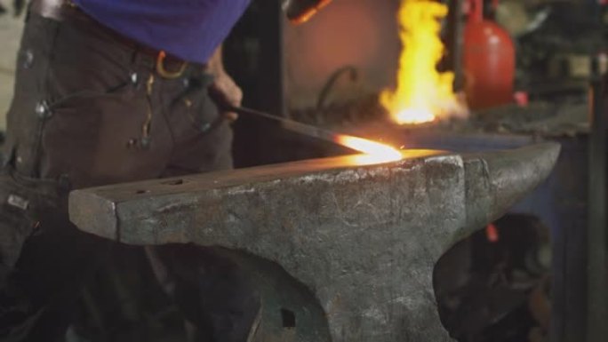 男性铁匠在铁砧上锤击金属制品的特写镜头，背景为火花和炽热的锻造