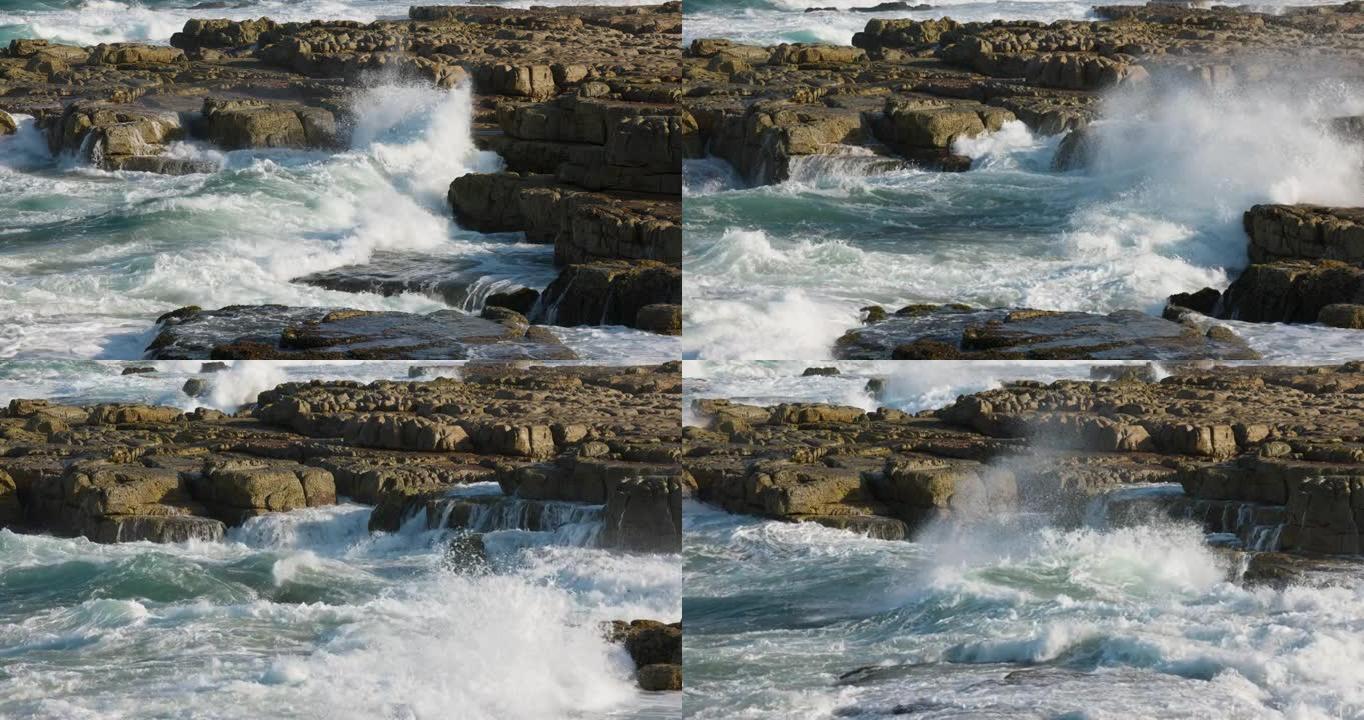 在岩石海岸线上冲破岩石的波浪的空中慢动作视图