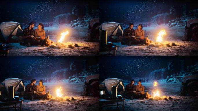 快乐情侣大自然晚上在峡谷露营，使用坐在篝火旁的数字平板电脑。两个旅行的人在互联网社交媒体上发布鼓舞人