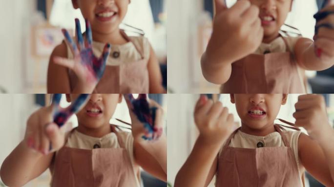 特写亚洲艺术家蹒跚学步的小女孩，穿着围裙，在家里的客厅里，她玩着颜色，用可爱的微笑看着相机。