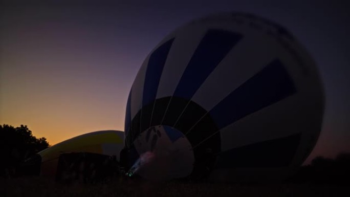 黎明时分，丙烷火焰在黑暗的田野中膨胀热气球