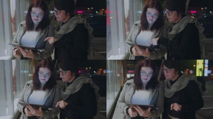 两名妇女在夜间在城市使用数字平板电脑
