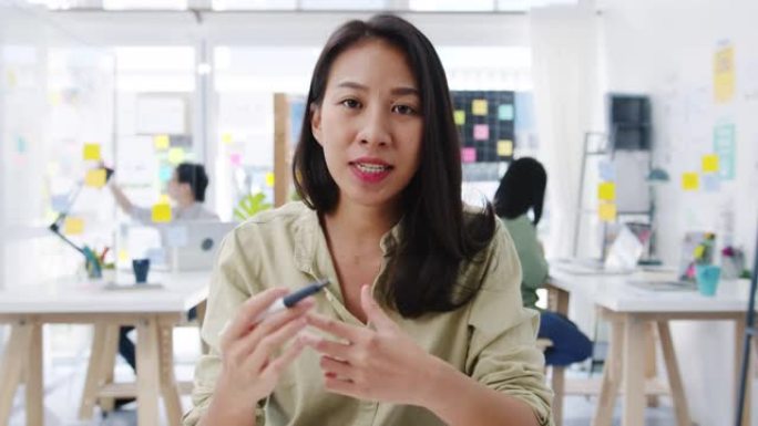 亚洲女商人在新的正常情况下进行社交距离预防病毒在办公室工作时向朋友介绍有关视频通话计划的摄像机演示。