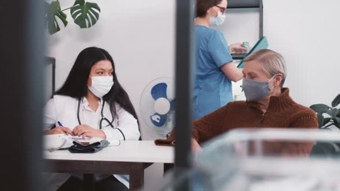 年轻友好的女性多民族医生穿着实验室外套咨询高级病人，在诊所医院办公室微笑。