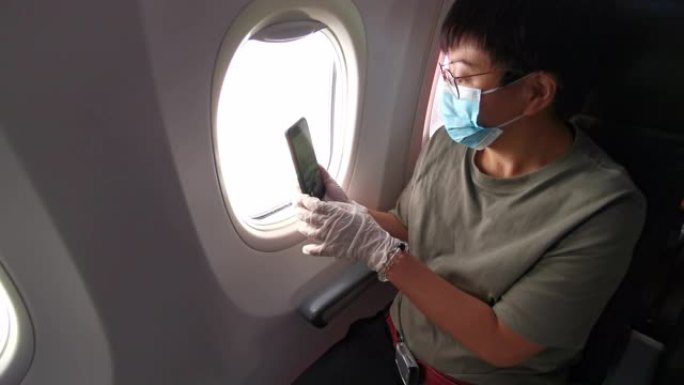 一名亚裔中国中年妇女在商业飞机的乘客座位上，戴着口罩和橡胶手术手套望着窗外