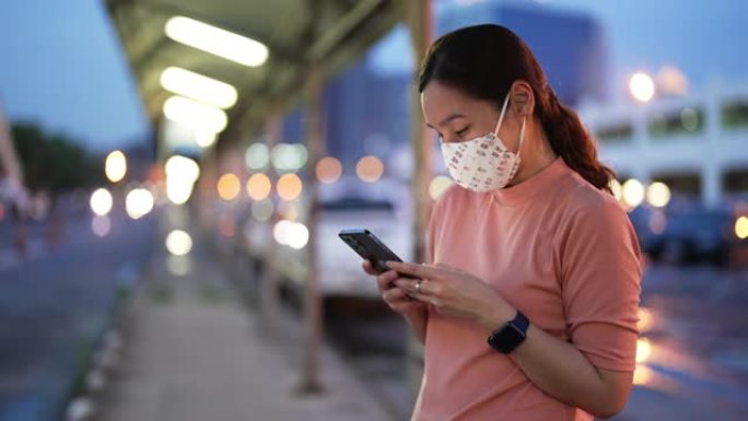 亚洲女子晚上戴口罩使用智能手机