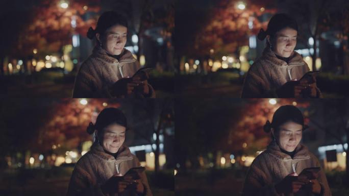 年轻漂亮的女人晚上在韩国使用智能手机。