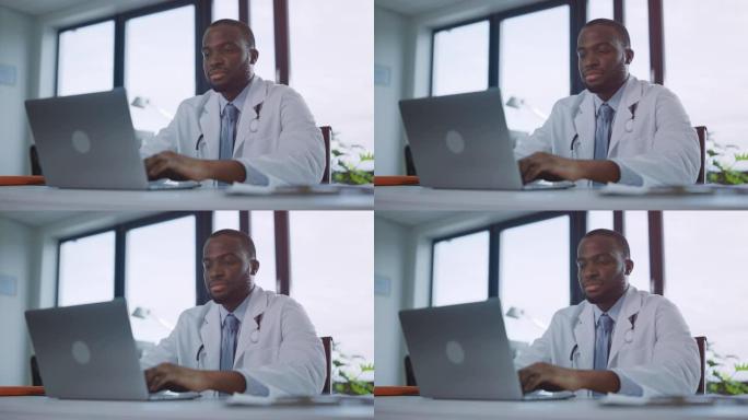 快乐的黑人男性家庭医生正在一家诊所的笔记本电脑上工作。穿着白大褂的医生正在医院办公室的桌子后面浏览病