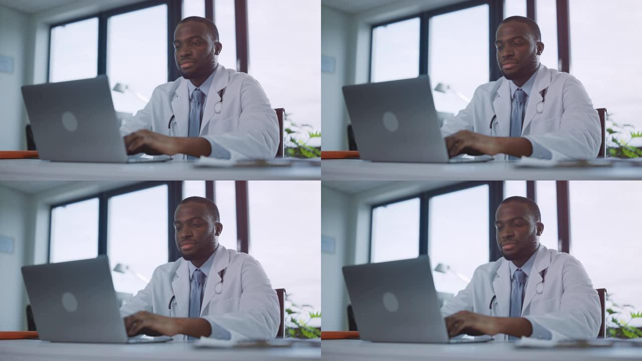 快乐的黑人男性家庭医生正在一家诊所的笔记本电脑上工作。穿着白大褂的医生正在医院办公室的桌子后面浏览病