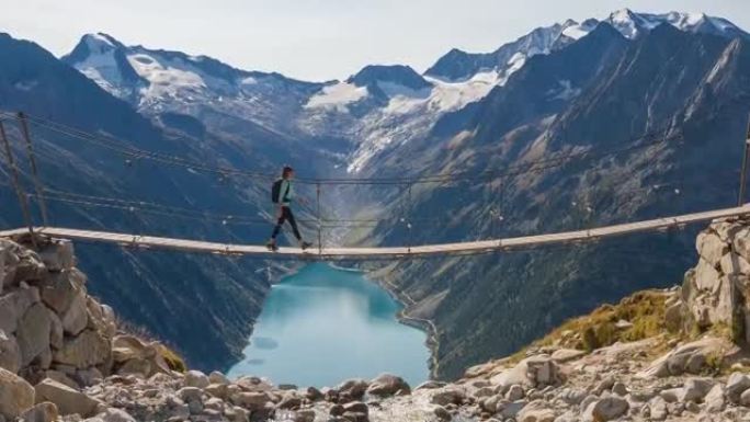 女徒步旅行者在山涧上的吊桥上行走，欣赏山谷湖和周围山脉的壮丽景色
