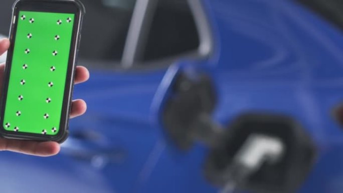 使用手机上的绿屏应用程序在家里的车库里的男人的特写检查电动汽车的电池电量-慢动作拍摄