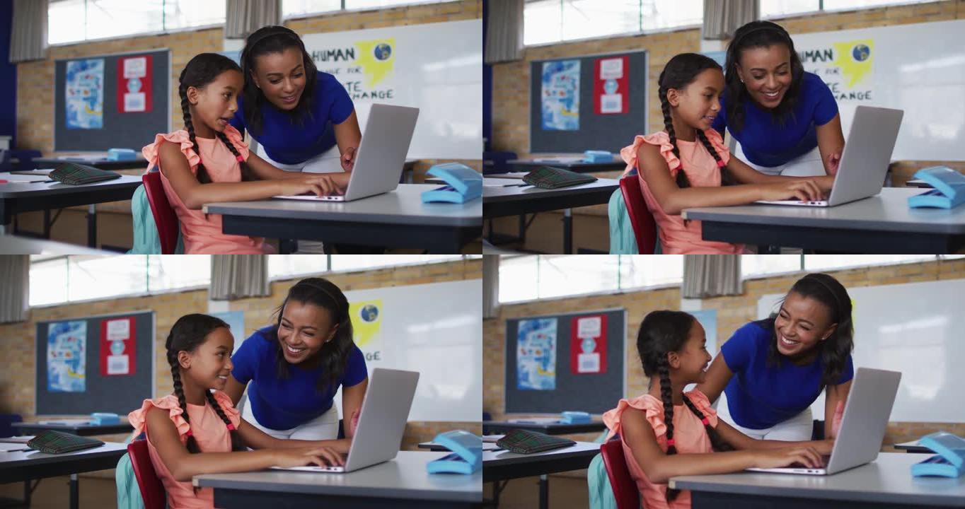 多元化的微笑女教师使用笔记本电脑帮助坐在教室里的女学生