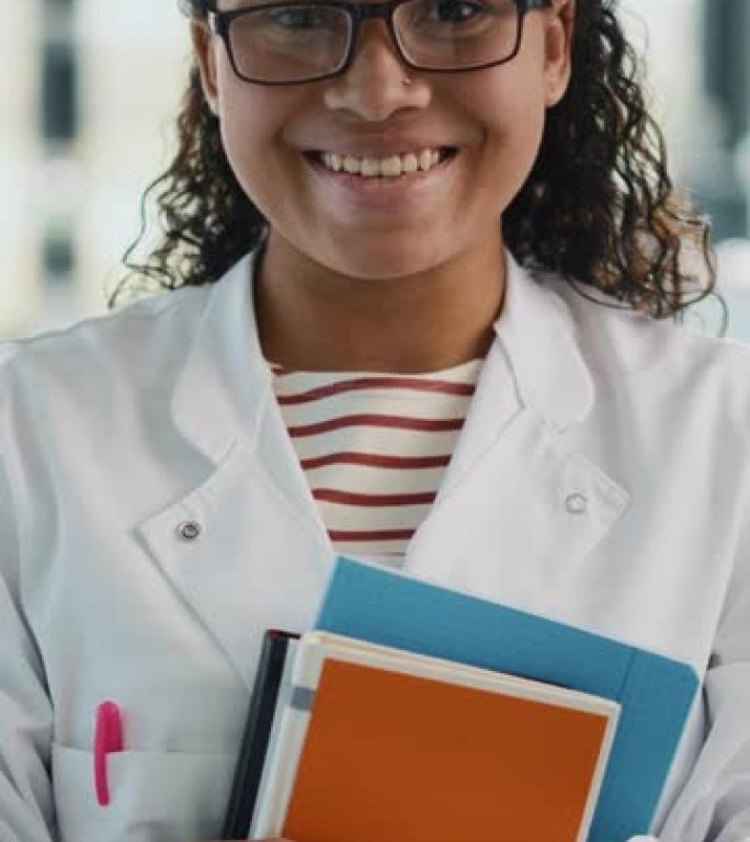 垂直屏幕截图。医学科学实验室: 美丽聪明的年轻黑人科学家的肖像，穿着白大褂和眼镜，拿着测试书，微笑着