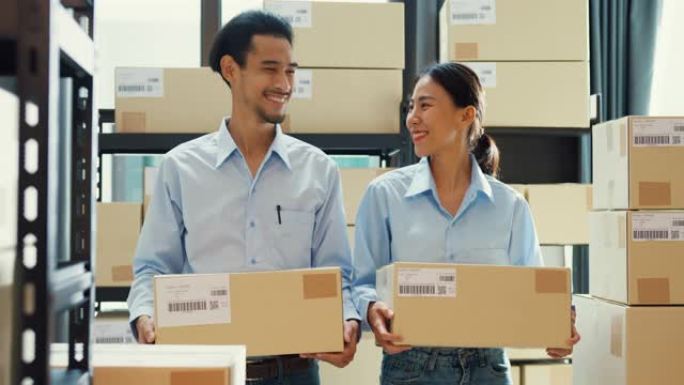 两个快乐的亚洲商业成功伙伴关系男女穿着制服衬衫背着纸板箱微笑着看着仓库里的相机。良好的合作效果，创业