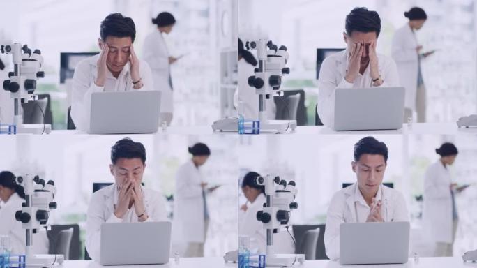 紧张的男性科学家在实验室里用笔记本电脑工作。年轻的研究生物学家因整天坐在办公桌前感到疲倦而头痛。生物