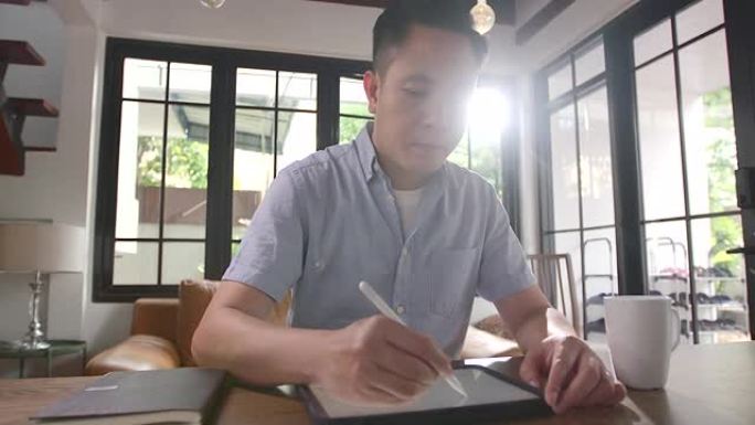 在检疫期间，一个亚洲年轻人坐在家里，用平板电脑工作。