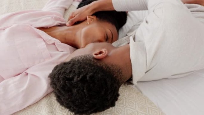快乐，爱情和情侣在卧室里亲吻和欢笑，在家里聚在一起。年轻的黑人男女躺在床上亲吻，微笑着为关心关系而高
