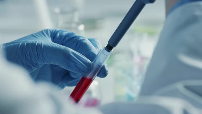 使用微量移液器关闭一名戴着手套的科学家的镜头，并在显微镜下拍摄红色化学液体或血液进行测试。用技术设备