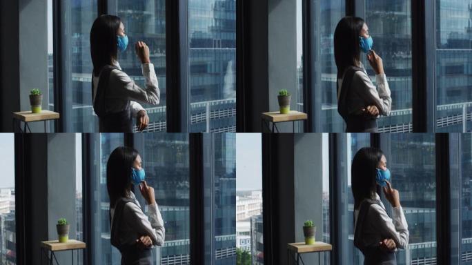 体贴的亚洲妇女戴着口罩在现代办公室看着窗外