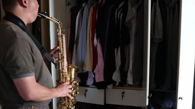 亚洲中国中年男子对着衣柜练习萨克斯管，以隔音，以减少声音打扰他公寓里的邻居