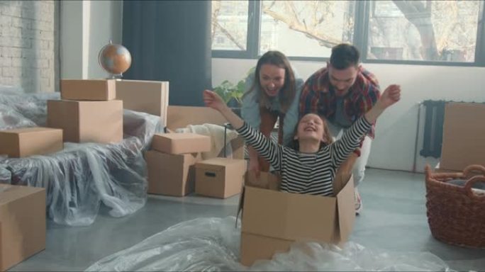 快乐的男人和女人在地板上的纸板箱里推兴奋可爱的少女庆祝搬进新的豪华公寓。