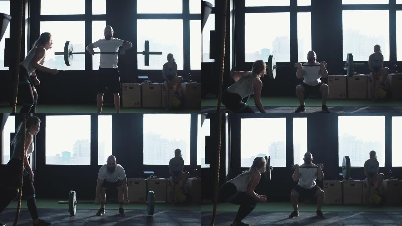 年轻的男健身房运动员举起沉重的杠铃的电影镜头，美丽的女教练在现代健身房为他提供支持