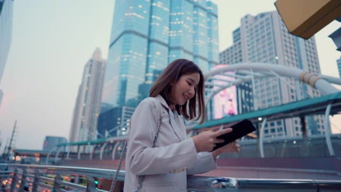 美丽的女人在城市的skywalk手持数字平板电脑。