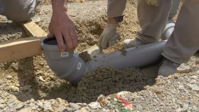 特写: 一群建筑商用混凝土掩埋了一根宽的塑料污水管。