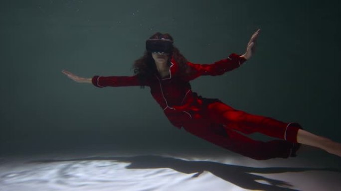 完整的虚拟现实体验。穿着红色睡衣的年轻美女使用VR耳机漂浮在水下慢动作。