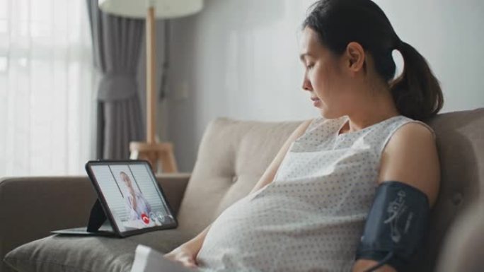 年轻的孕妇在数字平板电脑上与医生交谈并在家中检查血压