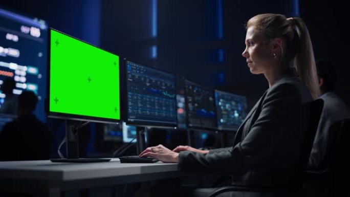 自信的女性数据科学家在大型基础设施控制室的绿色色度键屏幕计算机上工作。专家使用显示图表、信息的计算机
