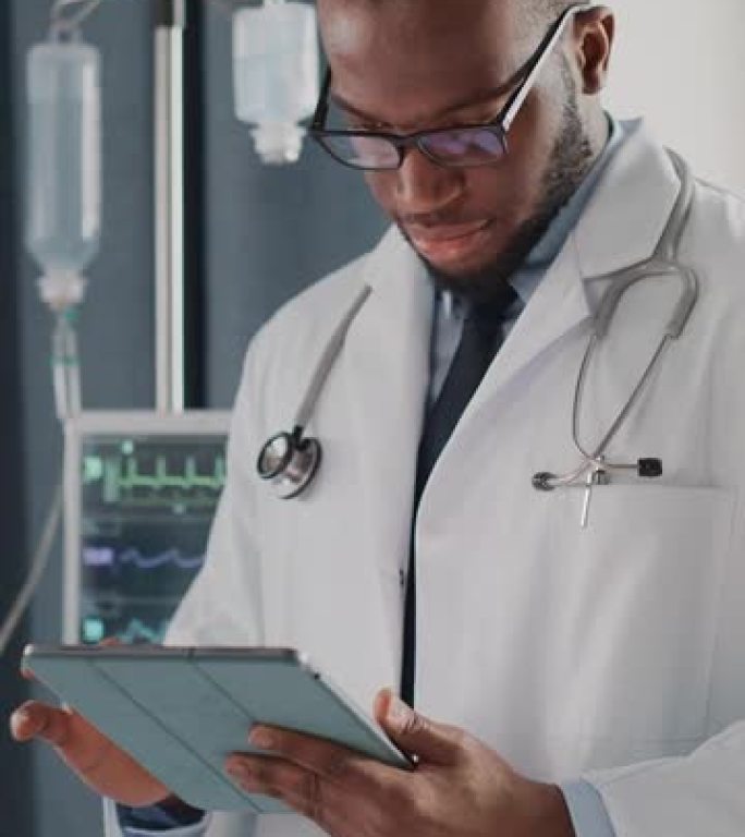 垂直屏幕。医院病房: 戴眼镜的英俊黑人医生使用数字平板电脑，检查患者的病史，最新医学研究。设备先进的