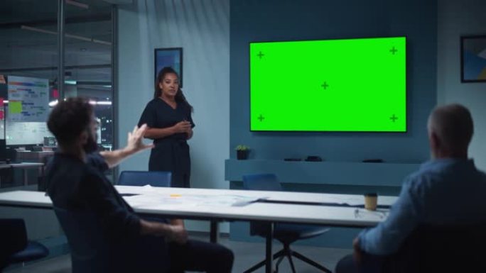 公司运营经理为一个高管团队举行会议演示。多民族女性使用带有水平绿屏模拟显示的宽电视机。人们在商务办公