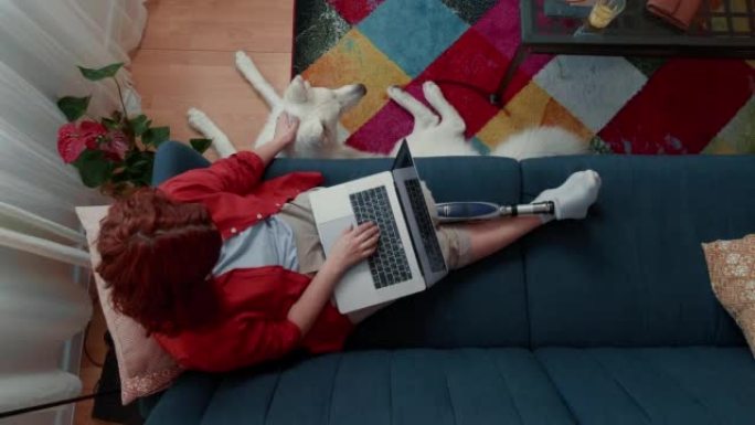 顶视图快乐的残疾女商人，用笔记本电脑和大狗一起在家工作的假肢机器人。
