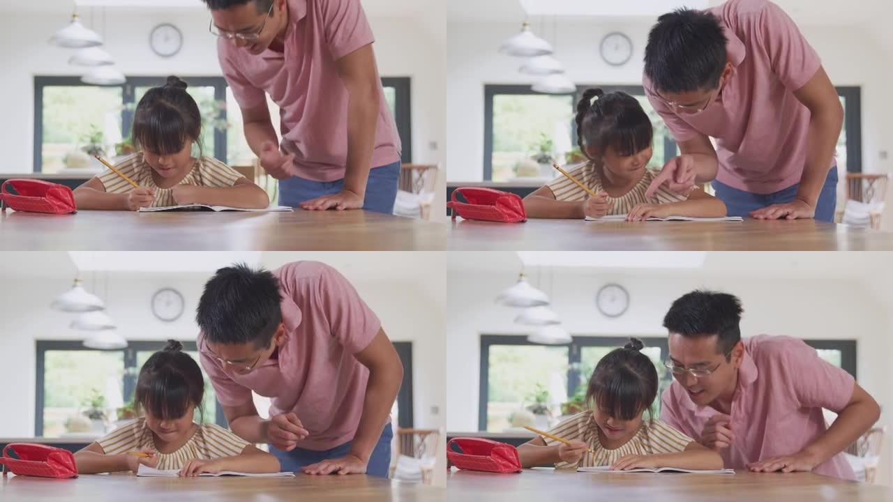 亚洲父亲帮助在家上学的女儿在厨房的餐桌上写书