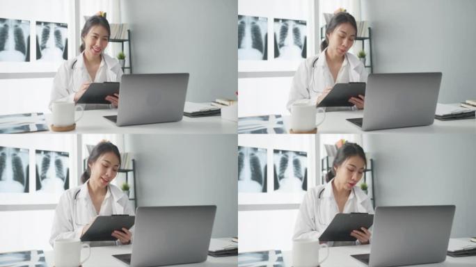 年轻的亚洲女士医生穿着白色医疗制服，配有听诊器，使用电脑笔记本电脑通话视频电话会议，病人在诊所或医院