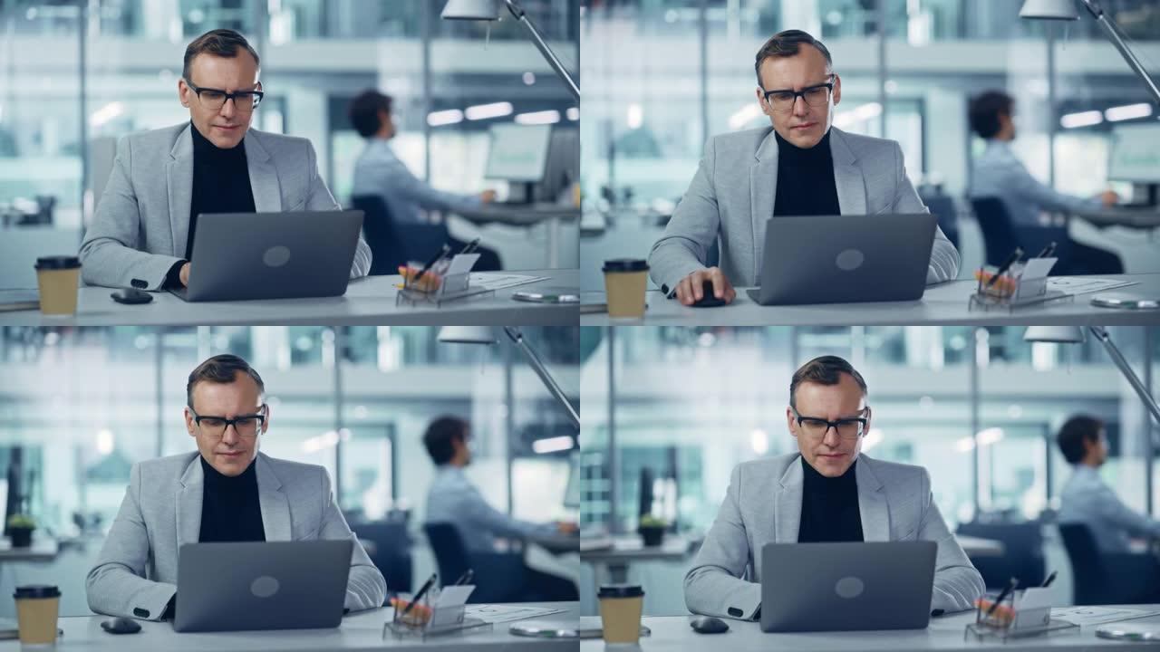 现代办公室: 成功的中年商人穿着西装和眼镜在办公桌前的笔记本电脑上工作的肖像。严肃、自信、时尚的公司