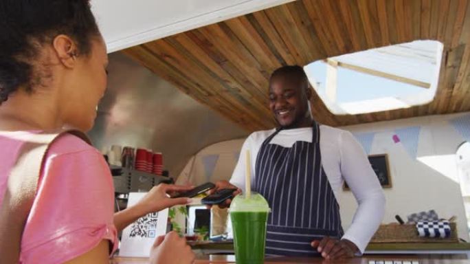快乐的女顾客支付微笑的非洲裔美国男性餐车老板通过智能手机