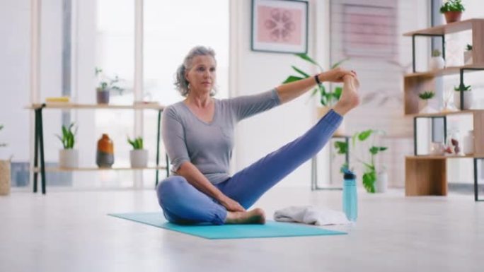 资深女性在家客厅的垫子上做瑜伽。活跃的女人做普拉提，以坐姿伸展双腿，同时练习平衡和冥想，以保持健康的
