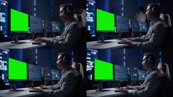 客户支持专家在大型基础设施控制室的绿色色度键屏幕计算机上与耳机进行对话。专家使用显示图表的计算机。与