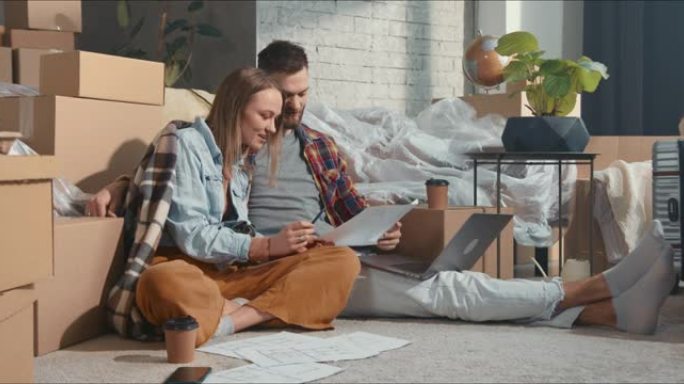 搬进新家。快乐的年轻男女使用笔记本电脑，在拆卸盒中查看公寓计划蓝图表。
