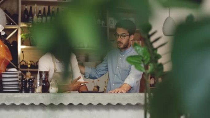 4k视频片段，一个英俊的年轻人与他的服务员站在咖啡馆里并使用数字平板电脑
