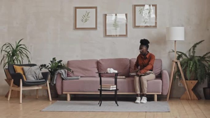 黑人妇女坐在沙发上并通过视频通话在线学习
